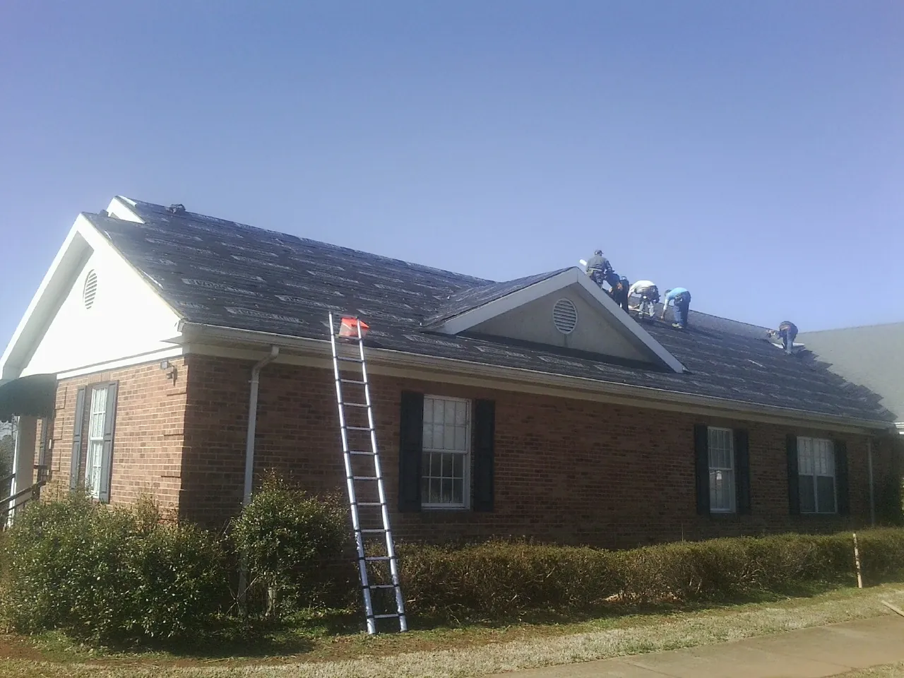 Crew tearing shingles off a brick ranch roof with a ladder set — Emergency Roof Repair work by our crew in Bennington