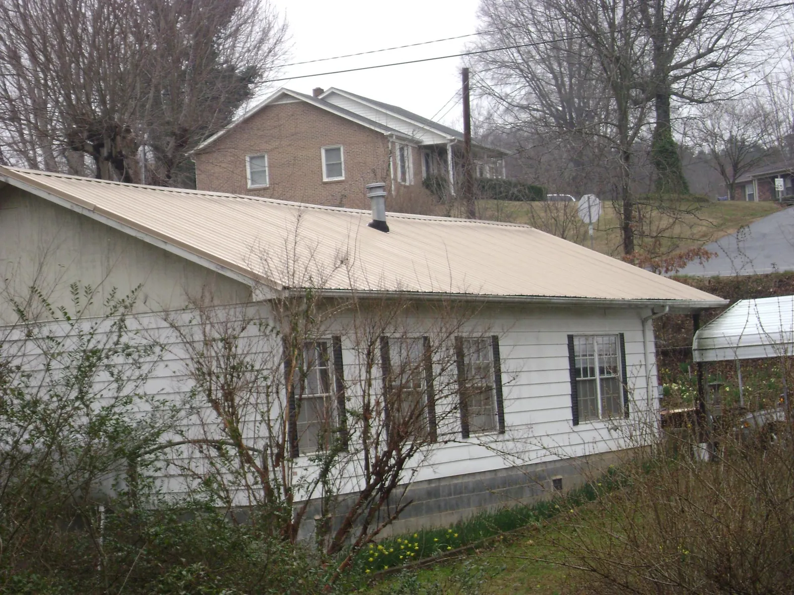 Tan metal roof on a white sided house set into a hillside — Commercial Roofing by Roofing Brothers in Bennington